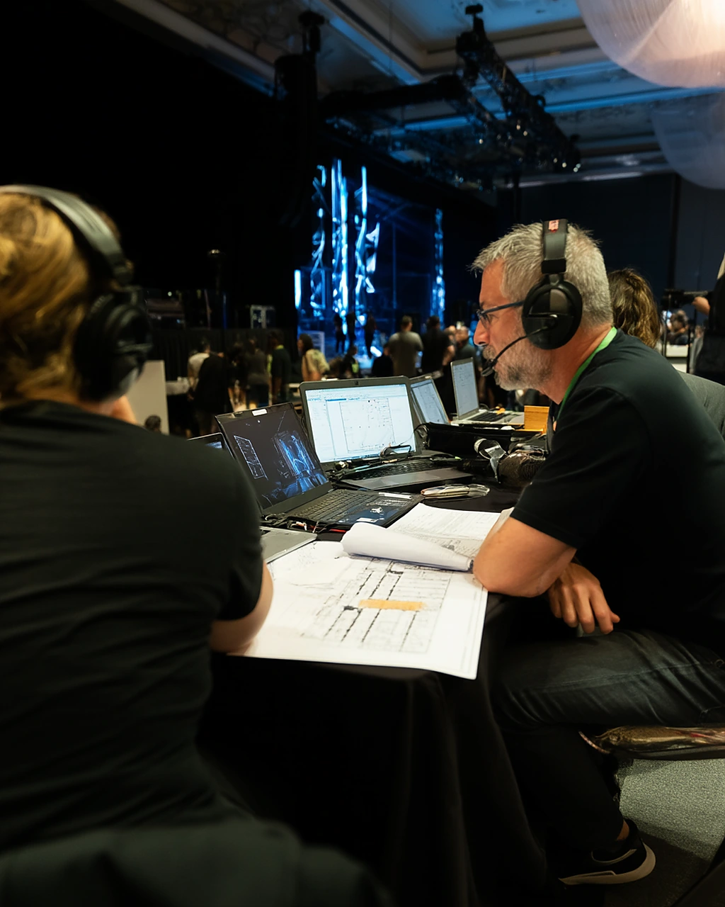 Event producers running cue sheets and screens from a backstage command table before doors open